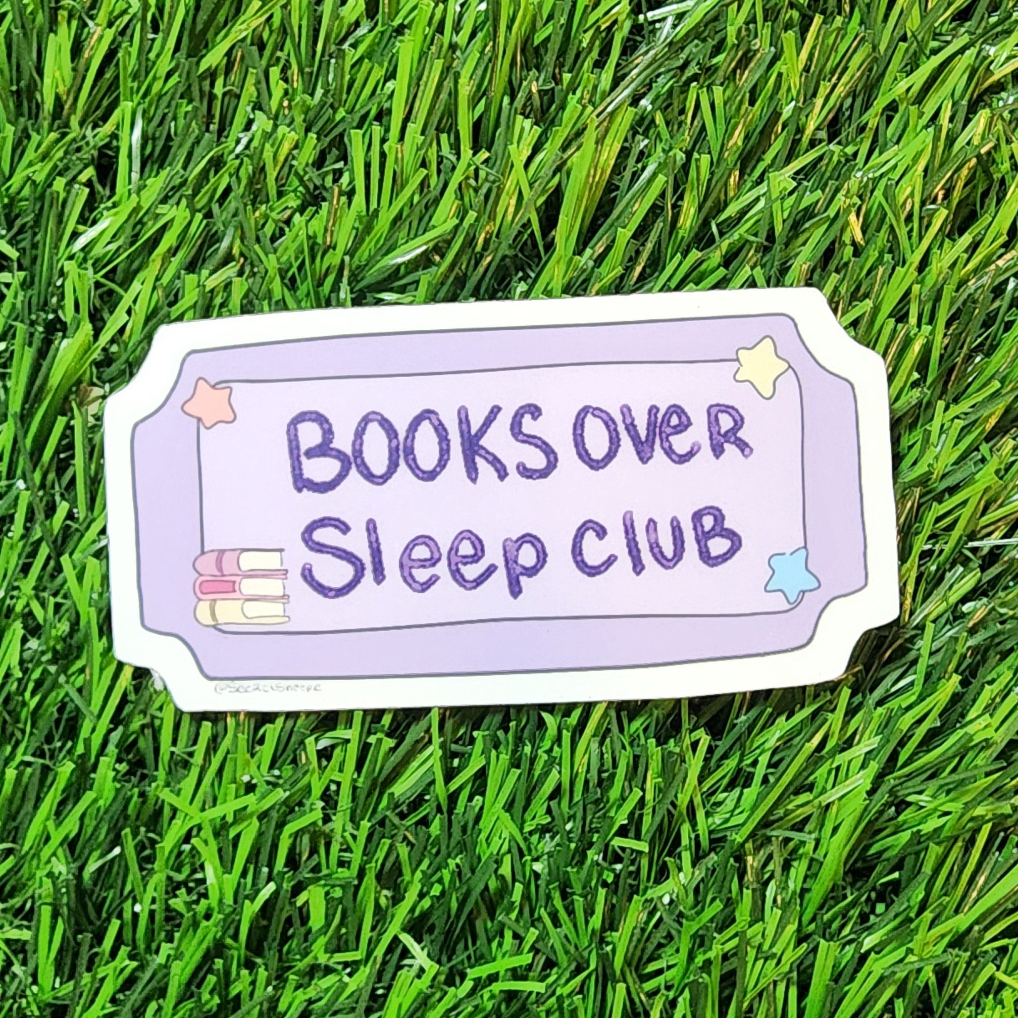 Sticker with 'Books Over Sleep Club' text on a grass background