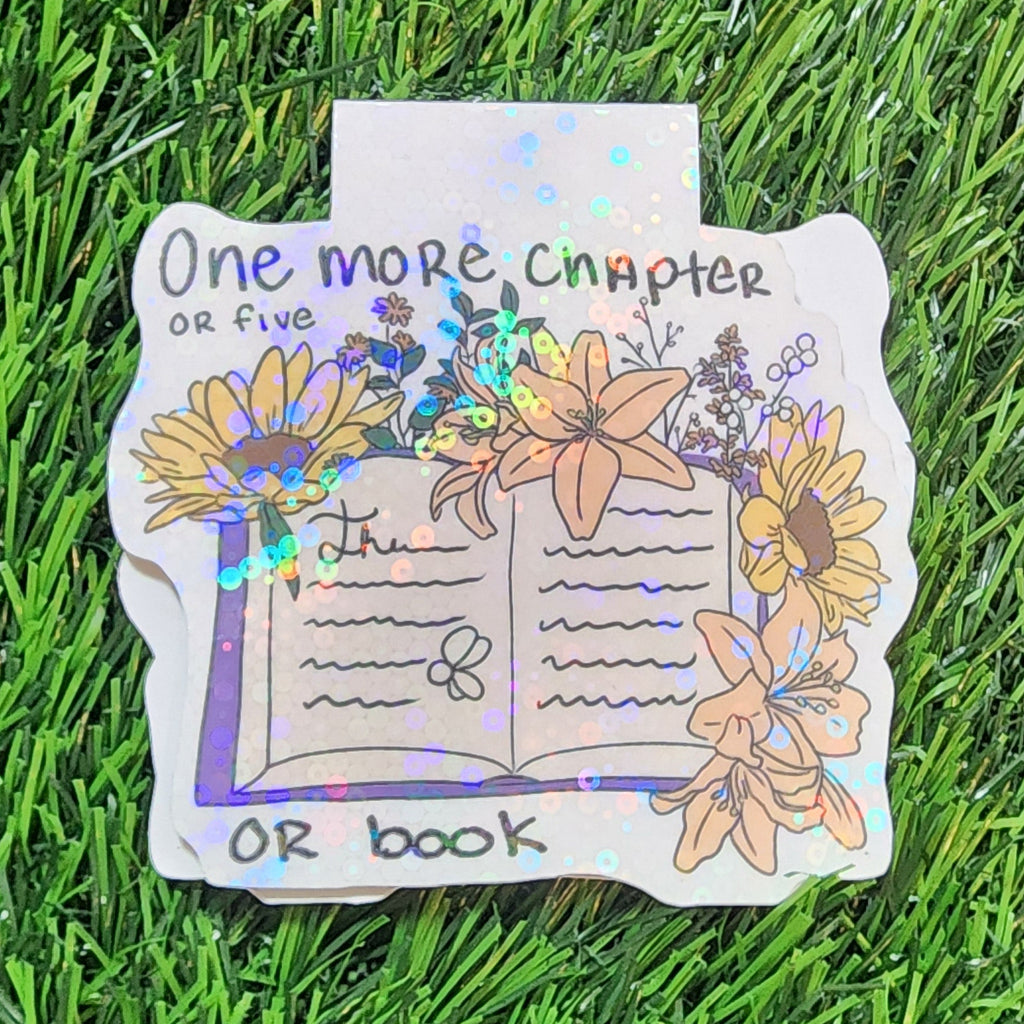 Decorative magnetic bookmark with floral design and text on a grass background