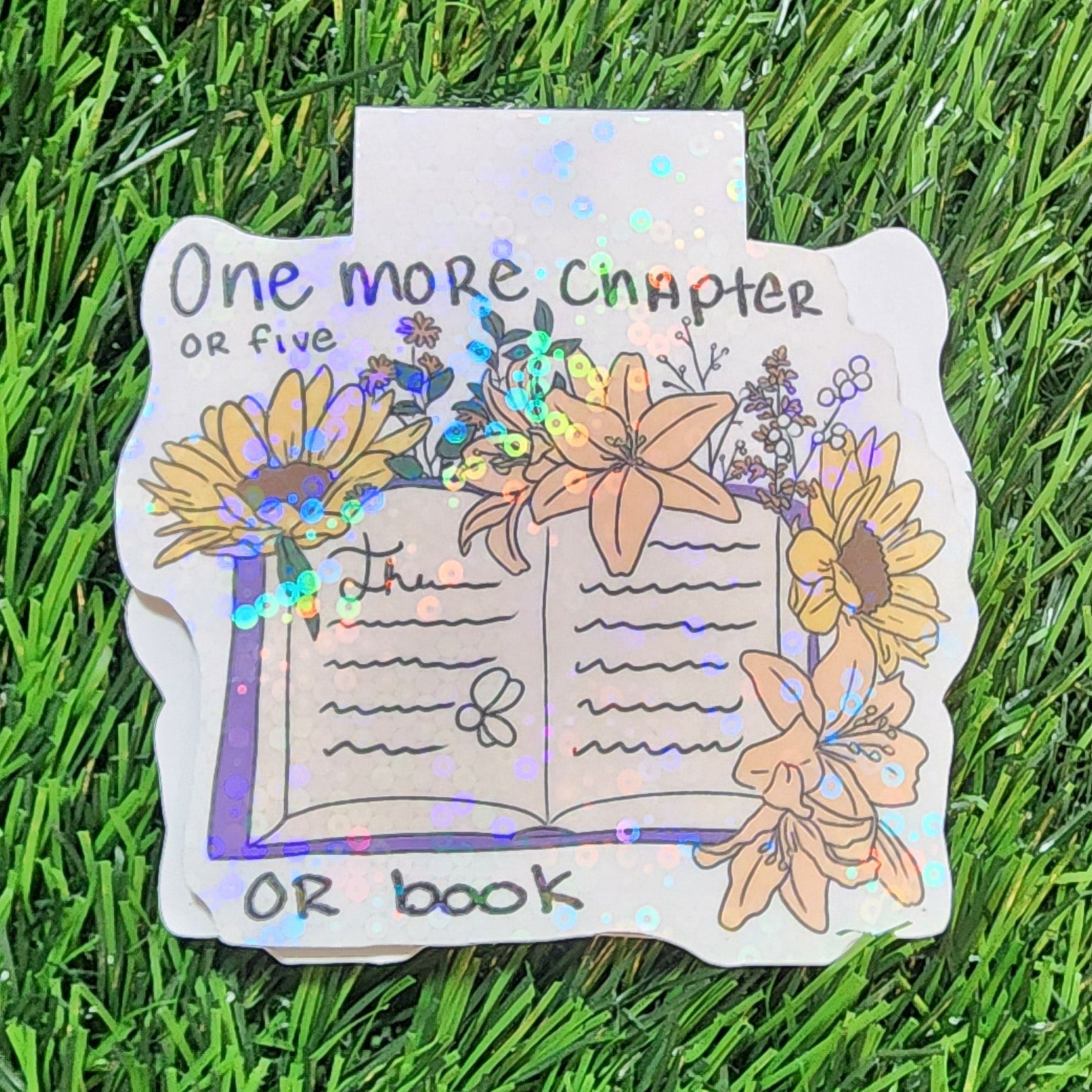 Decorative magnetic bookmark with floral design and text on a grass background